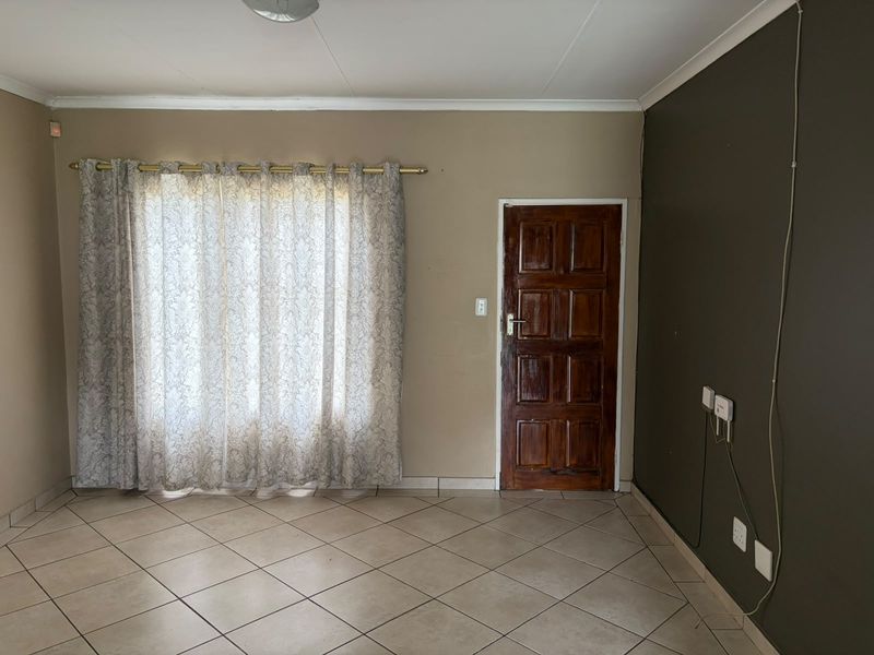 An empty living room featuring tiled flooring, a wooden entrance door, and neutral wall tones, providing a blank canvas for personalization.