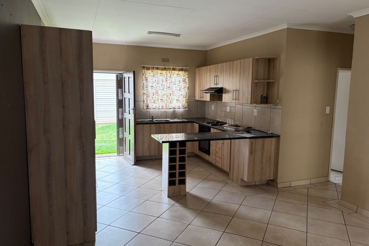A functional kitchen featuring light wood-finish cabinetry, granite countertops, built-in cooking appliances, and tiled flooring, with direct access to the rear garden.