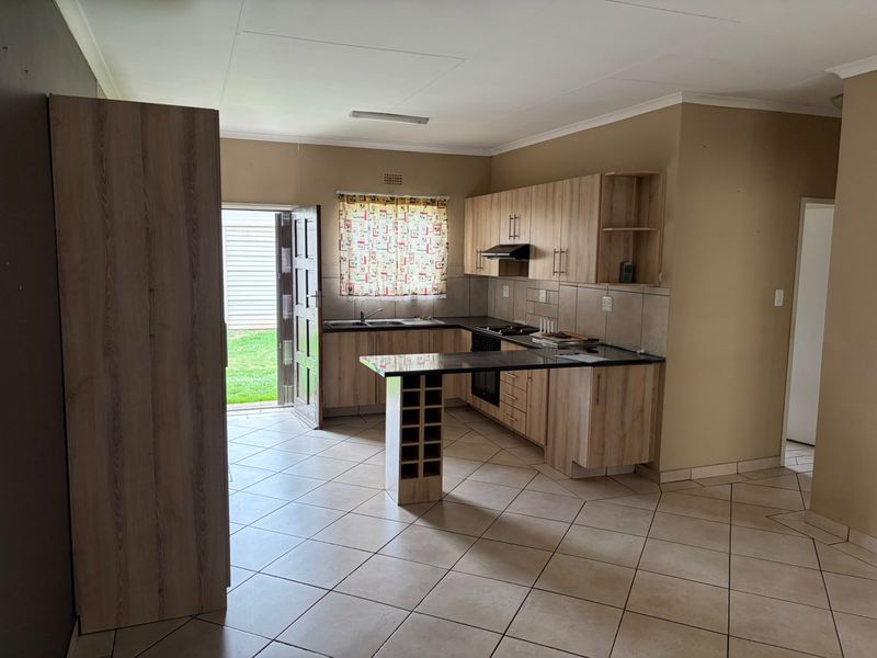 A functional kitchen featuring light wood-finish cabinetry, granite countertops, built-in cooking appliances, and tiled flooring, with direct access to the rear garden.