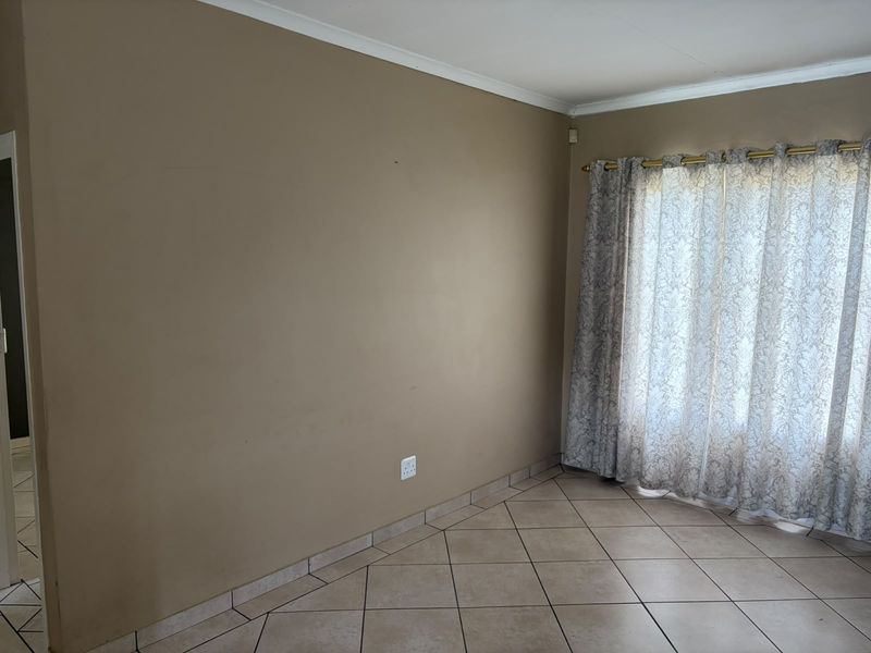 An empty living room featuring neutral wall paint, tiled flooring, and a large window with installed curtain rods.