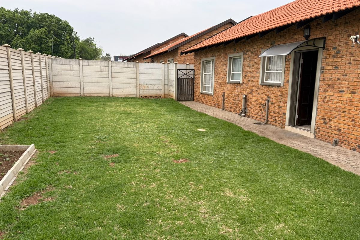 A private rear garden featuring a lawn, paved walkway, and face brick townhouse exterior with a tiled roof and boundary walling.