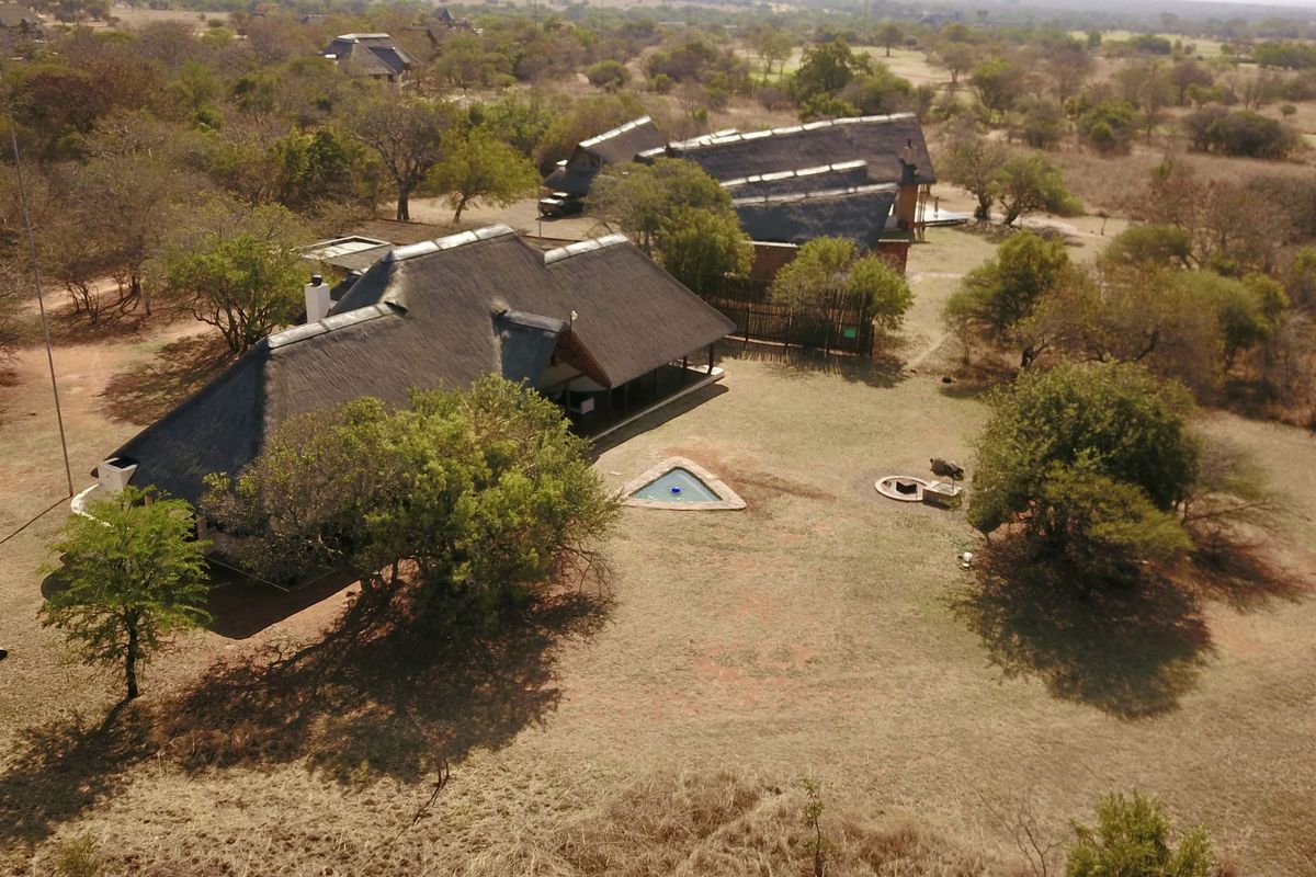 Aerial view of a lodge property featuring multiple thatched-roof buildings, a swimming pool, and a fire pit set within a natural bushveld landscape.