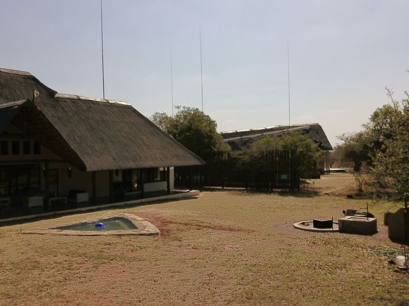 Rear view of a lodge featuring a thatched roof, covered patio, small plunge pool, and a boma fire pit area in a natural setting.