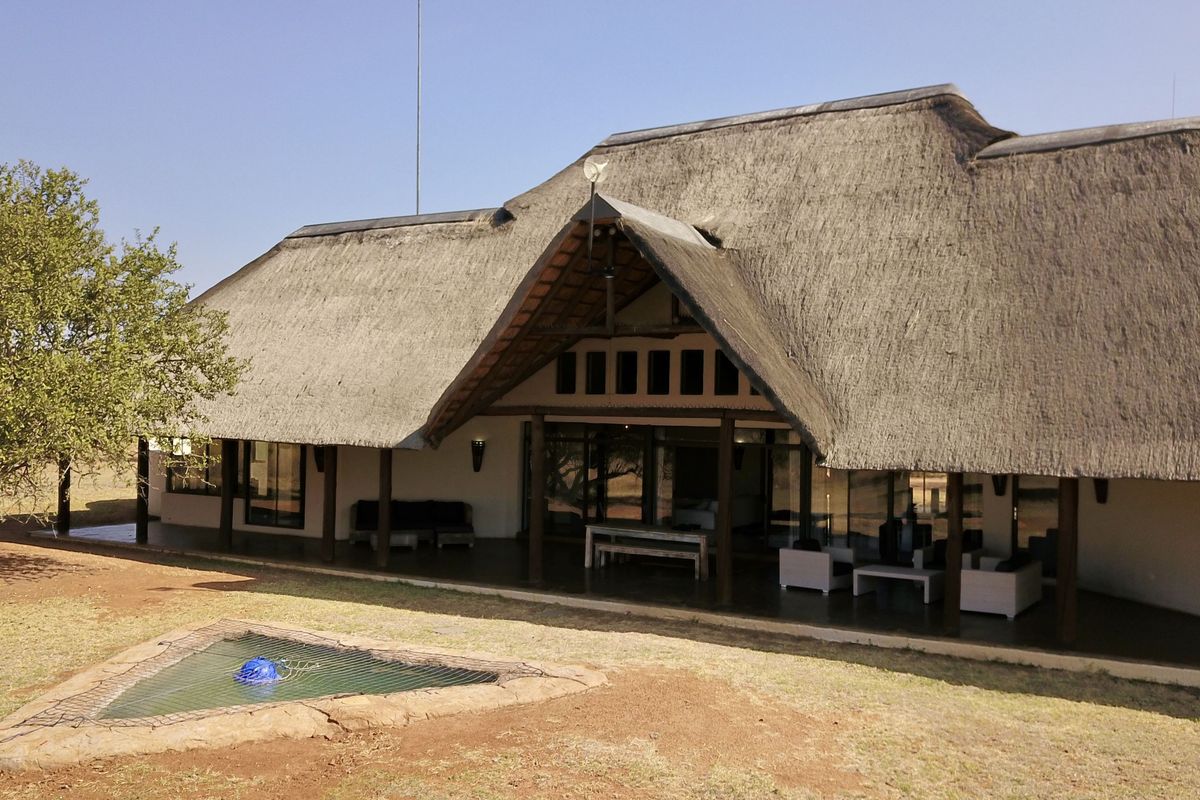 Rear view of a lodge featuring a traditional thatched roof, expansive covered patio, and large sliding glass doors overlooking the natural landscape.