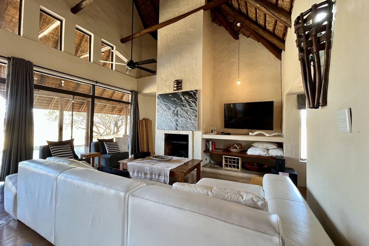 Spacious living room featuring a high vaulted thatched ceiling with exposed timber beams, a central fireplace, and large sliding doors opening to the outdoors.