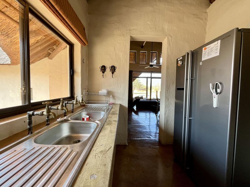 A rustic scullery area featuring a double stainless steel sink, concrete countertop, and exposed plumbing, leading through to the main living space.