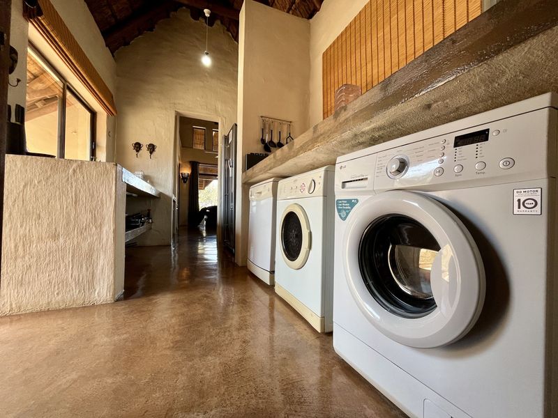 A rustic laundry area featuring polished concrete flooring, a built-in concrete countertop, and exposed thatch roofing with timber rafters.
