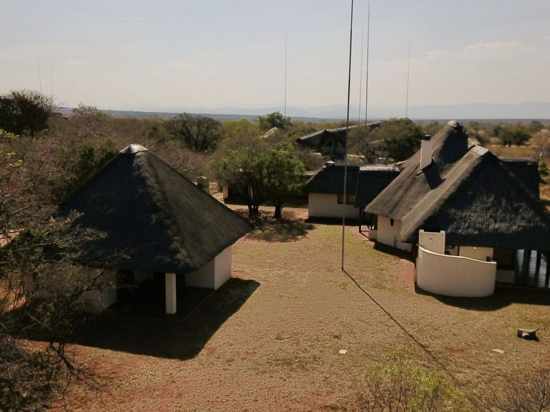 Aerial view of a lodge property featuring multiple structures with traditional thatched roofs set within a natural bushveld landscape.