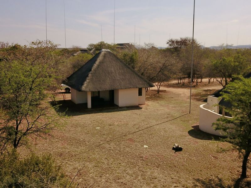 Aerial view of a lodge unit featuring a traditional thatched roof and a covered patio area set within a natural bushveld landscape.