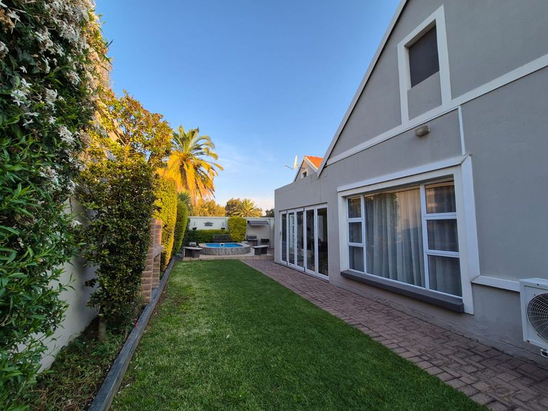 Rear exterior view of the townhouse featuring a manicured lawn, paved walkway, built-in braai area, and a swimming pool.