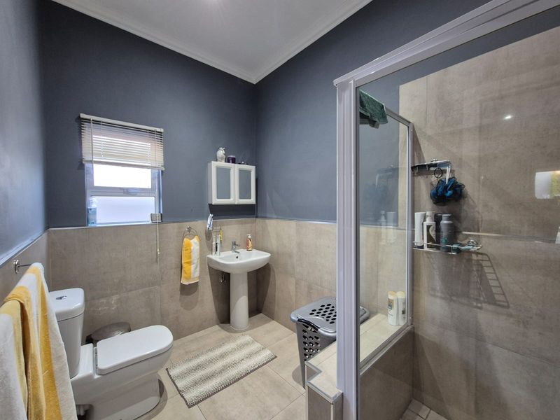 A functional bathroom featuring a pedestal basin, a glass-enclosed shower, a toilet, and neutral wall tiling with contrasting dark grey upper walls.