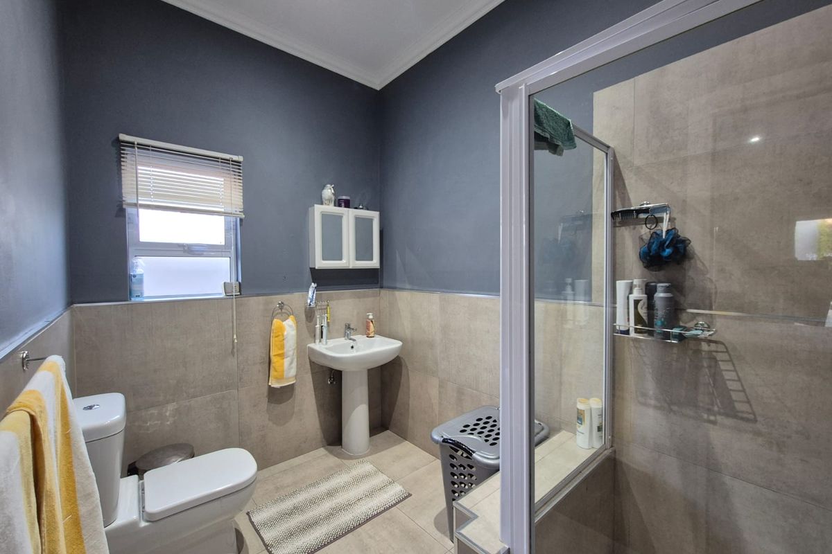 A functional bathroom featuring a pedestal basin, a glass-enclosed shower, a toilet, and neutral wall tiling with contrasting dark grey upper walls.