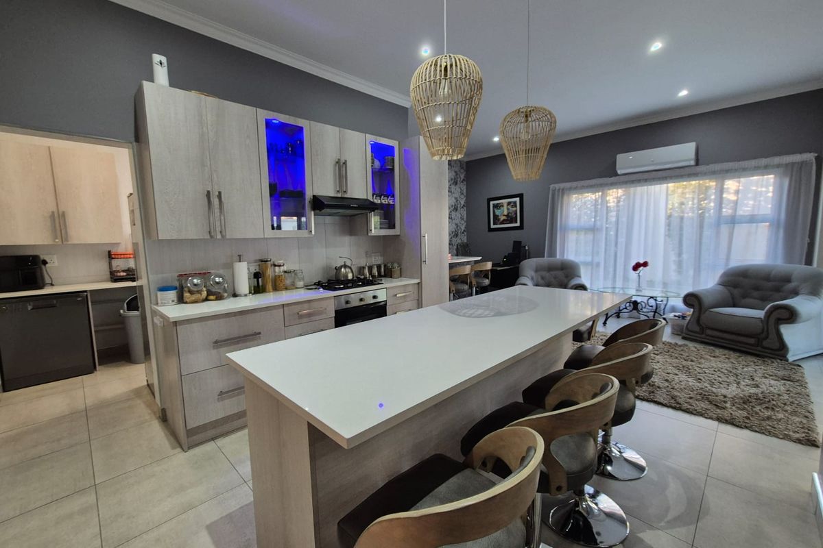 Modern open-plan kitchen and living area featuring a central island, contemporary cabinetry, gas hob, and tiled flooring with integrated air conditioning.