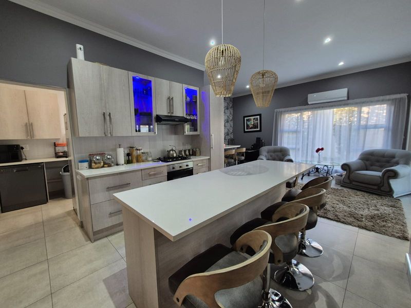 Modern open-plan kitchen and living area featuring a central island, contemporary cabinetry, gas hob, and tiled flooring with integrated air conditioning.