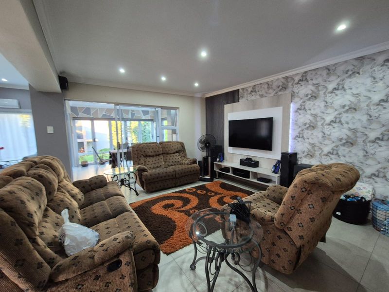 Spacious living room featuring tiled flooring, recessed downlights, a modern feature wall with integrated media unit, and sliding glass doors leading to the patio.