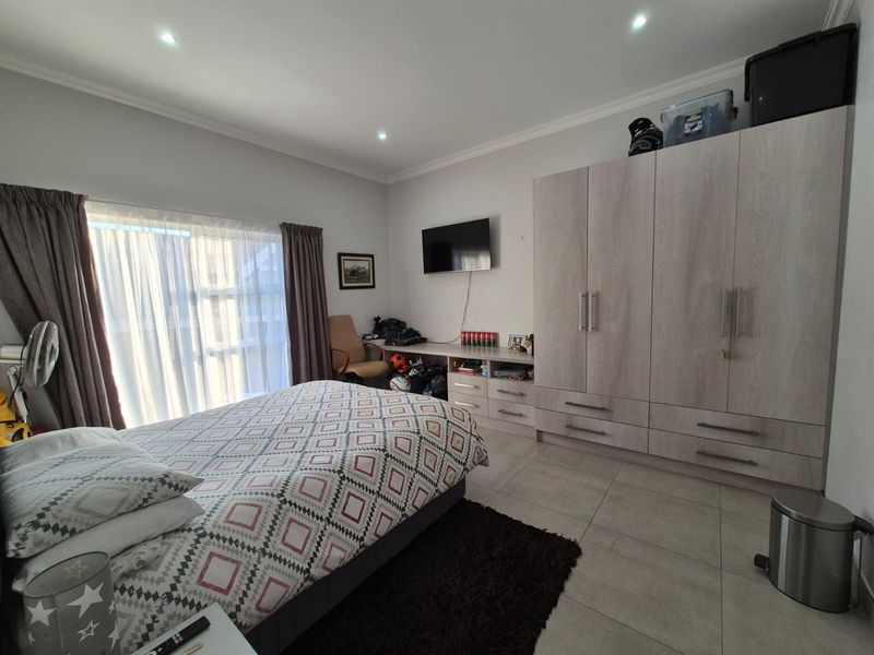 A well-maintained bedroom featuring neutral tiled flooring, recessed downlights, and extensive built-in cabinetry with an integrated desk area.