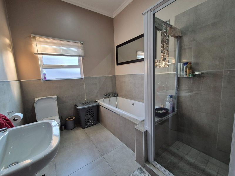 A well-maintained bathroom featuring a built-in bathtub, separate glass-enclosed shower, pedestal basin, and neutral floor-to-wall tiling.