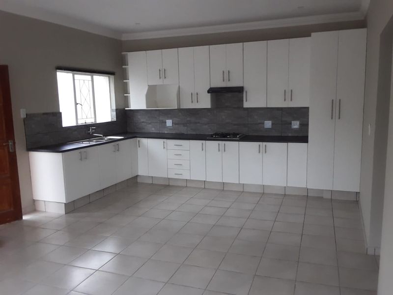 A clean, empty kitchen featuring white built-in cabinetry, dark countertops, a gas hob with extractor, and neutral tiled flooring.