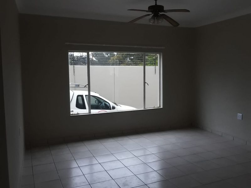 An empty living room featuring neutral tiled flooring, a ceiling fan, and a large window providing natural light.