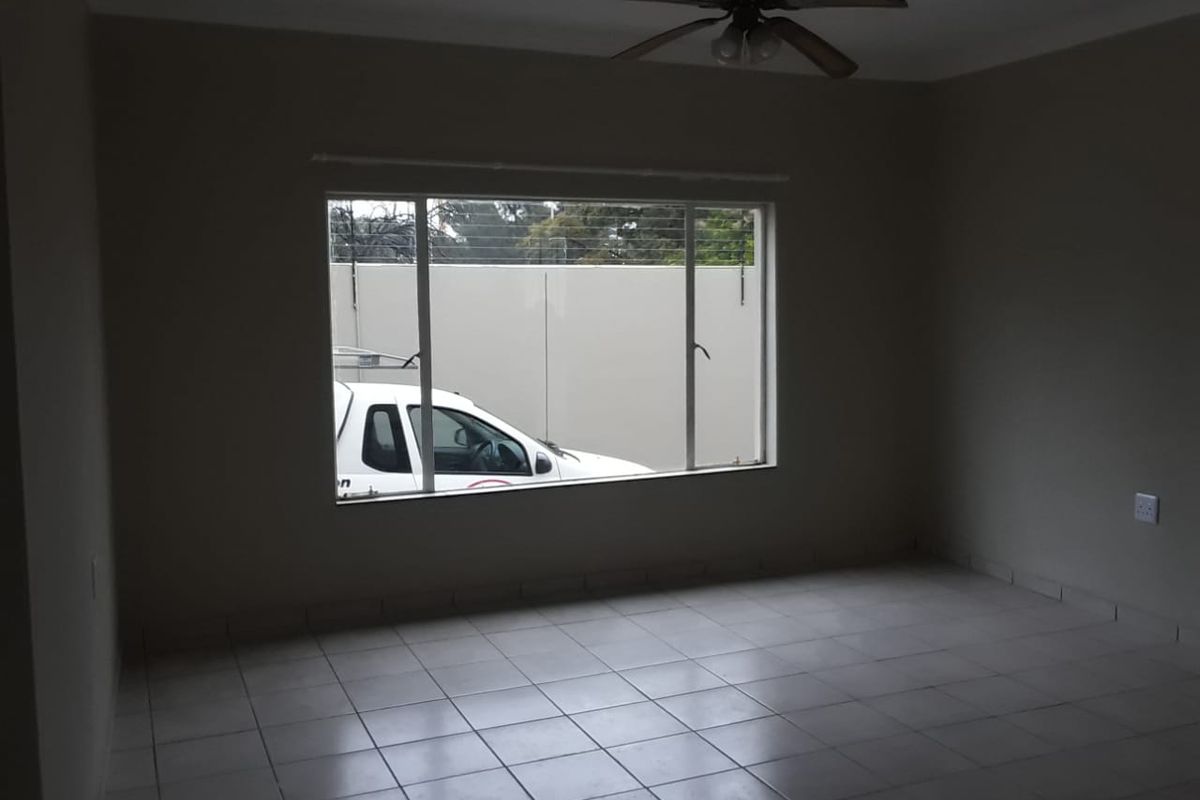 An empty living room featuring neutral tiled flooring, a ceiling fan, and a large window providing natural light.