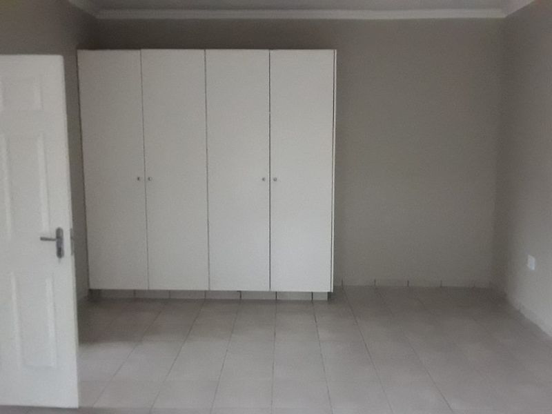 A clean, empty bedroom featuring neutral tiled flooring and white built-in cupboards, providing a blank canvas for personalization.