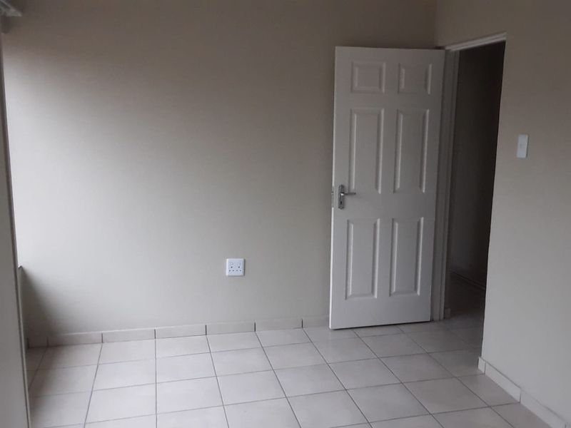 An empty bedroom featuring neutral wall paint, tiled flooring, and a white panel door, providing a clean and versatile space.