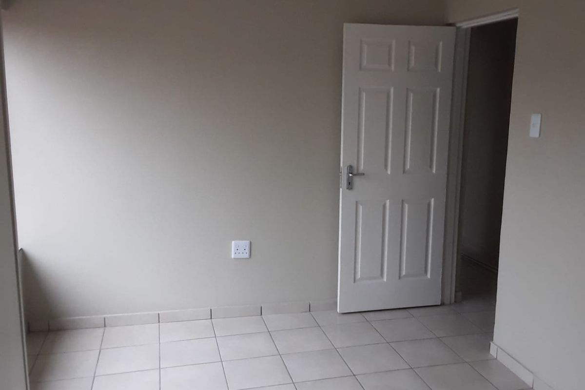 An empty bedroom featuring neutral wall paint, tiled flooring, and a white panel door, providing a clean and versatile space.