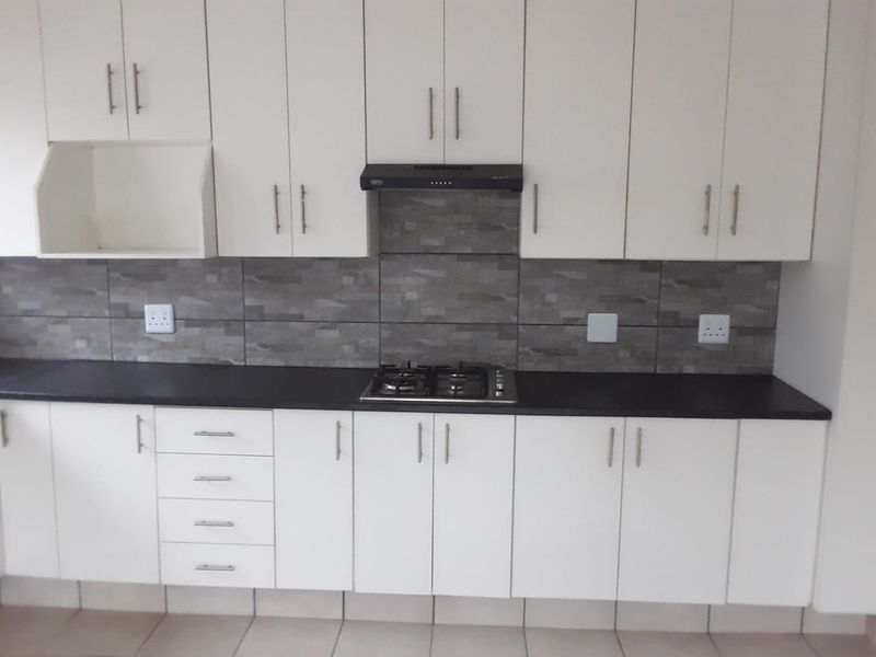 A clean, functional kitchen featuring white cabinetry, a dark countertop, a gas hob with an extractor fan, and a modern tiled backsplash.