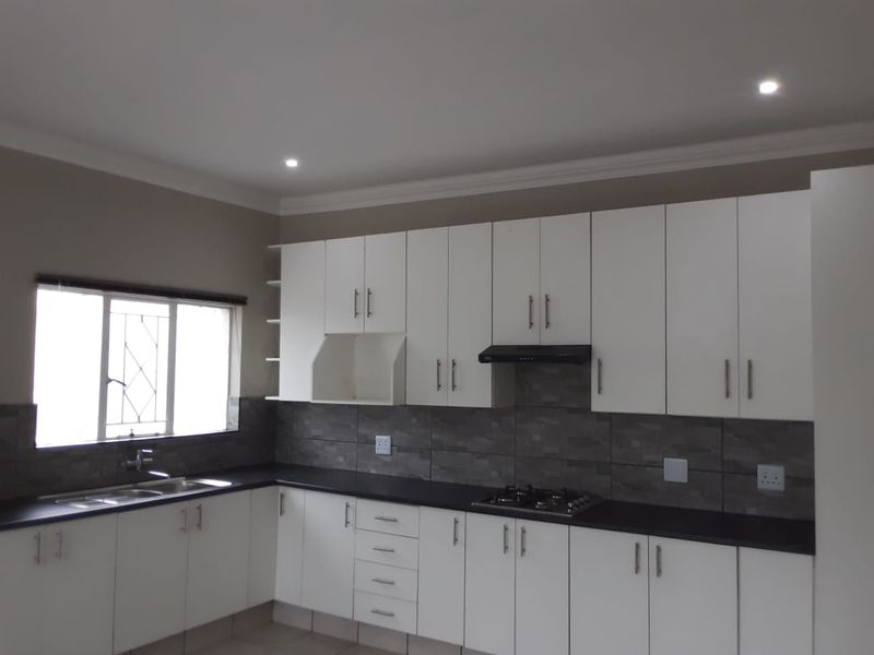 A clean, modern kitchen featuring white cabinetry, dark stone countertops, a gas hob with extractor, and a tiled backsplash.