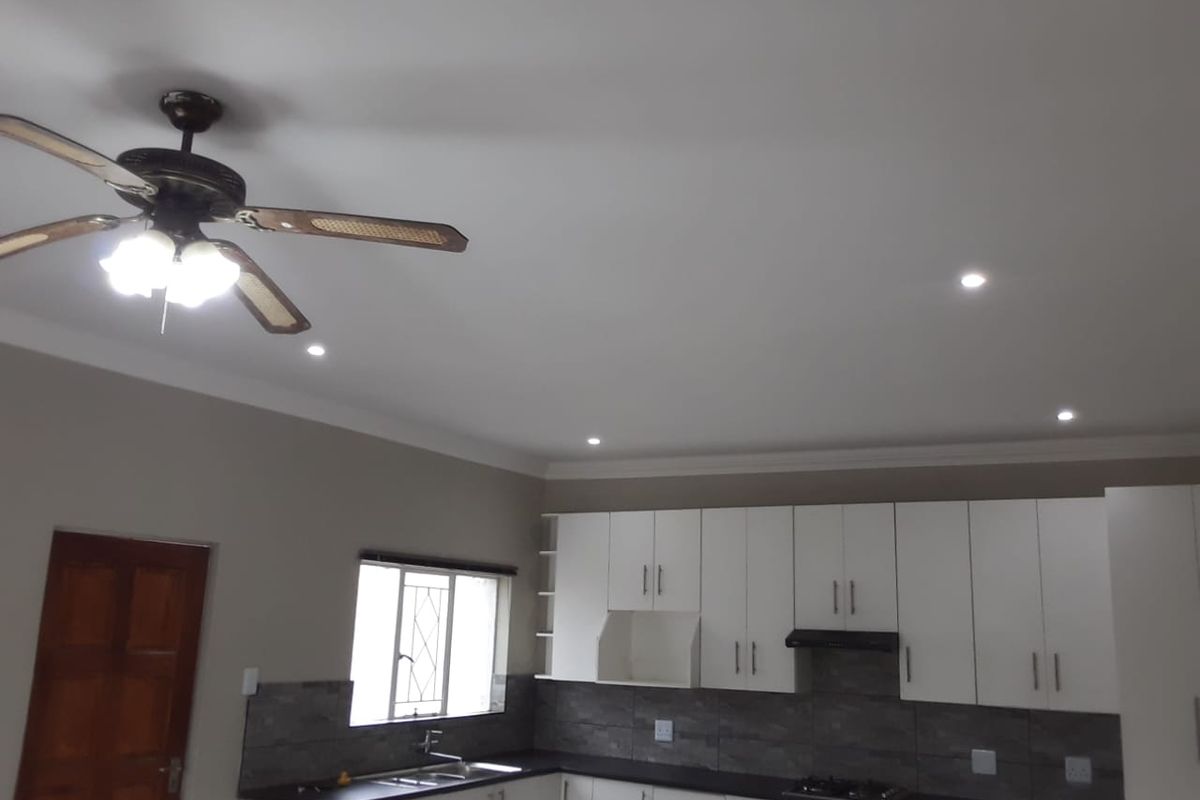 Modern kitchen featuring white cabinetry, dark countertops, tiled backsplash, integrated hob, extractor fan, and recessed ceiling lighting.