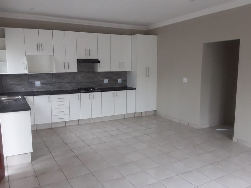 A clean, empty kitchen featuring white built-in cabinetry, dark countertops, a gas hob with extractor, and neutral tiled flooring.