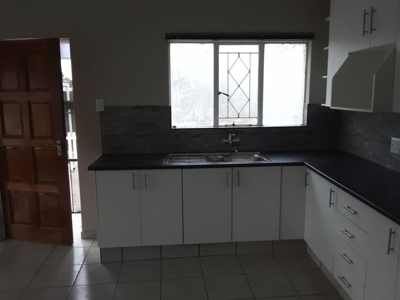 A functional kitchen featuring white cabinetry, dark countertops, a stainless steel sink, and tiled flooring, with direct access to an exterior door.