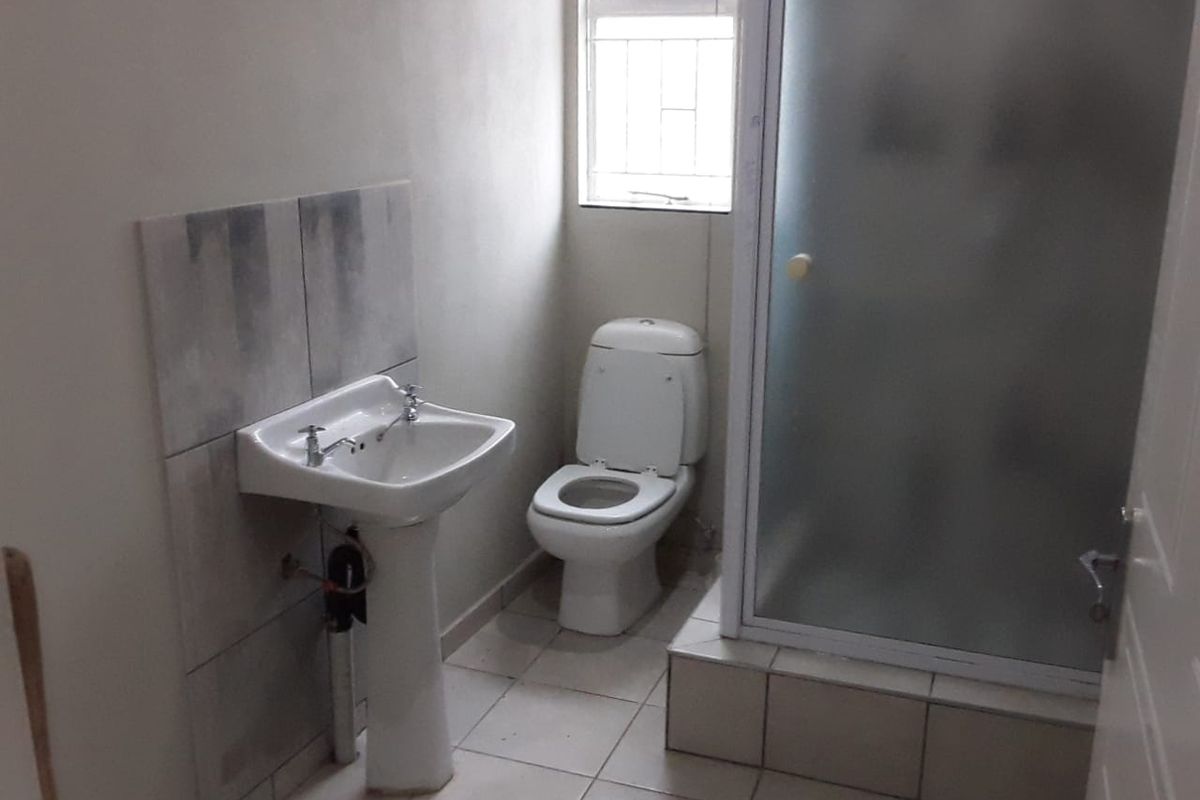 A functional bathroom featuring a pedestal basin, toilet, and a shower enclosure with a frosted glass door, finished with tiled flooring and splashbacks.