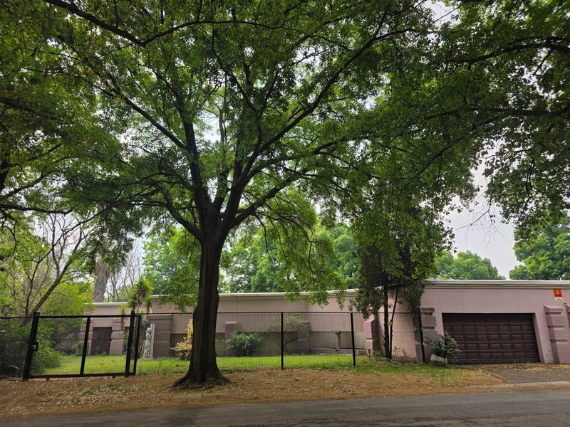 Front view of the property featuring a gated entrance, mature trees, and a garage, showcasing the exterior facade and street-facing boundary.