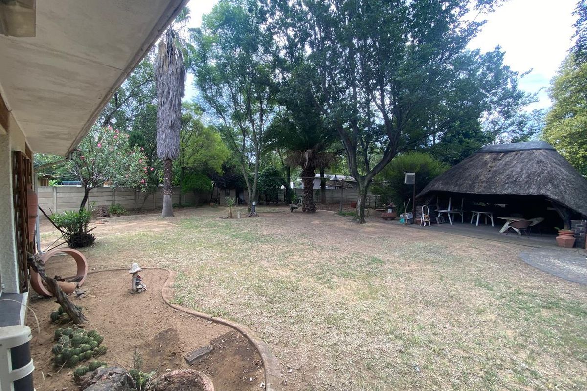 Spacious rear garden featuring a traditional thatch lapa, mature trees, and a precast concrete boundary wall, offering potential for landscaping improvements.