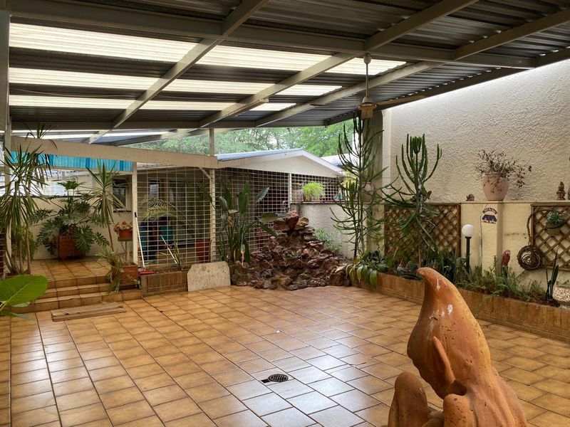 Spacious covered patio featuring tiled flooring, a built-in rock water feature, and raised planter beds, offering a versatile outdoor entertainment area.