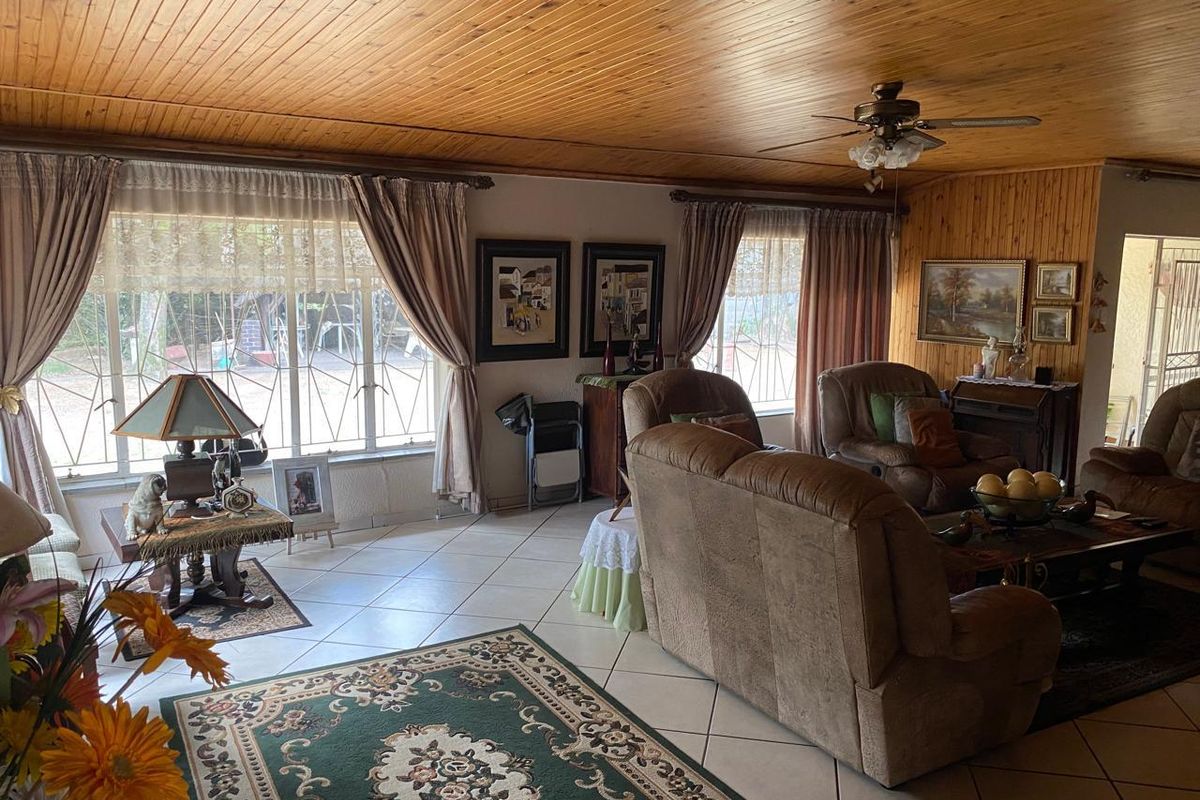 Spacious living room featuring timber-clad ceilings and walls, ceramic floor tiles, and large windows with security bars.