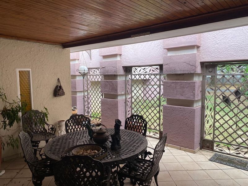 A covered patio area featuring a timber ceiling, tiled flooring, and decorative metal security screens, showing signs of wear on the masonry pillars.