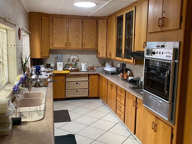 A functional kitchen featuring extensive wooden cabinetry, laminate countertops, a double basin sink, and a built-in oven with tiled flooring throughout.
