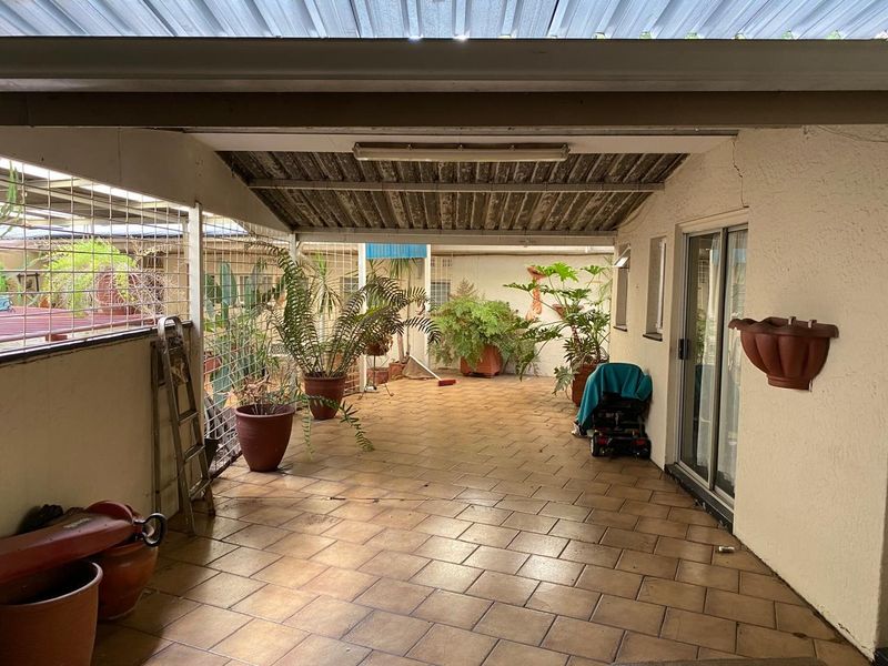 A covered outdoor patio area featuring tiled flooring, a corrugated roof, and sliding glass door access to the main dwelling.