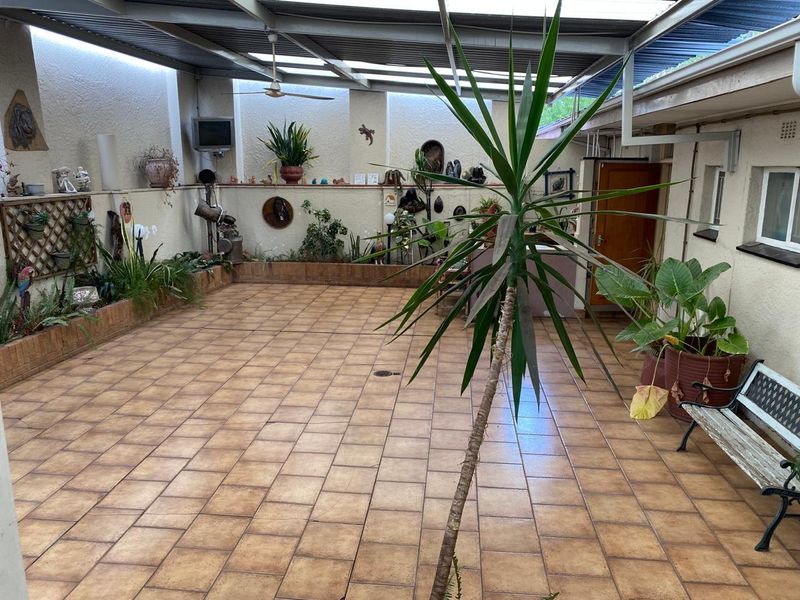 A spacious covered patio area featuring tiled flooring, built-in brick planter boxes, and a ceiling fan, offering a versatile outdoor entertainment space.