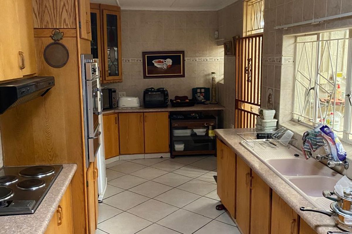 A functional kitchen featuring wooden cabinetry, laminate countertops, a double basin sink, and built-in cooking appliances with tiled flooring and splashbacks.