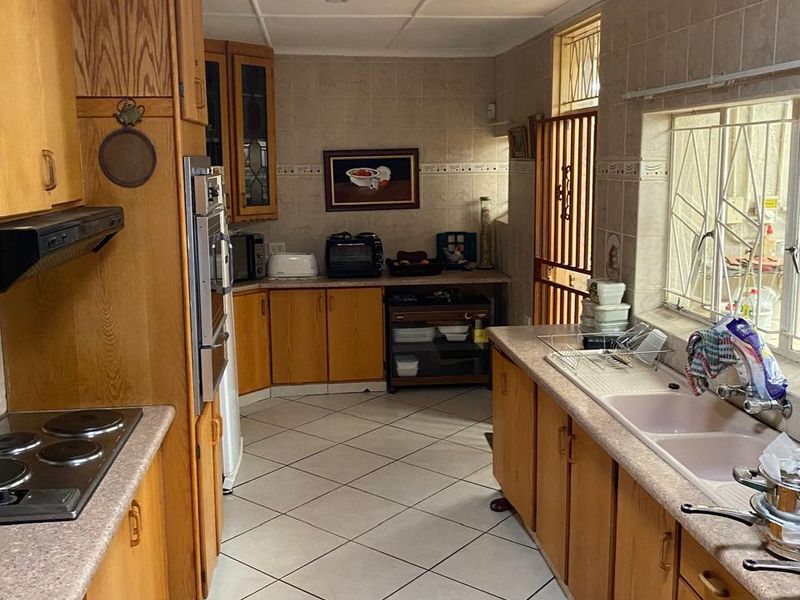 A functional kitchen featuring wooden cabinetry, laminate countertops, a double basin sink, and built-in cooking appliances with tiled flooring and splashbacks.