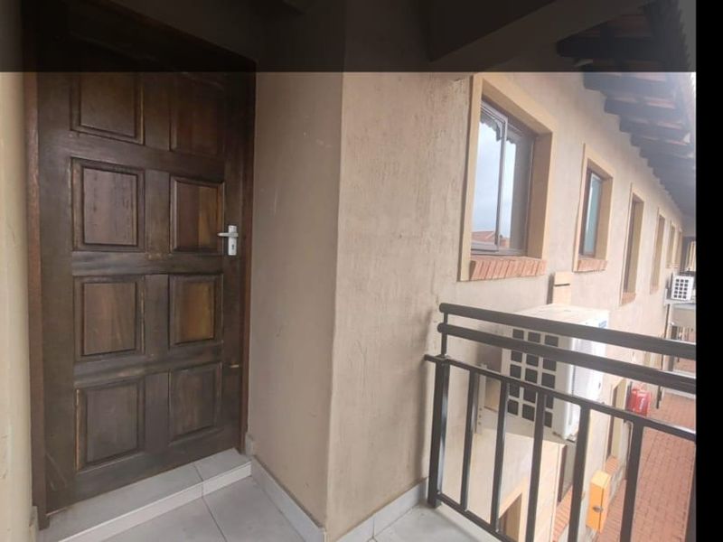 Exterior view of an apartment entrance featuring a wooden door, tiled landing, and metal safety railing.