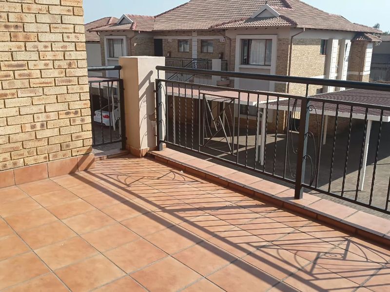 An open balcony featuring tiled flooring and a wrought iron balustrade, overlooking the apartment complex parking area.