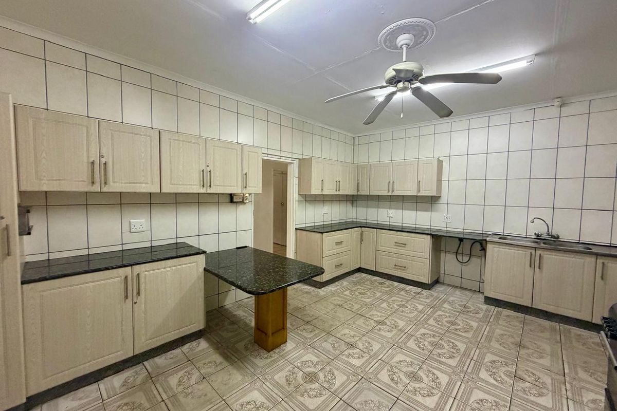 Spacious kitchen featuring extensive built-in cabinetry, granite countertops, double sink, and tiled finishes throughout, offering a functional layout ready for modernization.