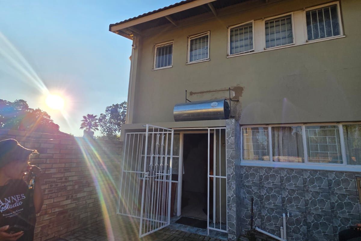 Rear exterior view of the townhouse featuring a paved courtyard, security gate, and a wall-mounted solar water heater unit.