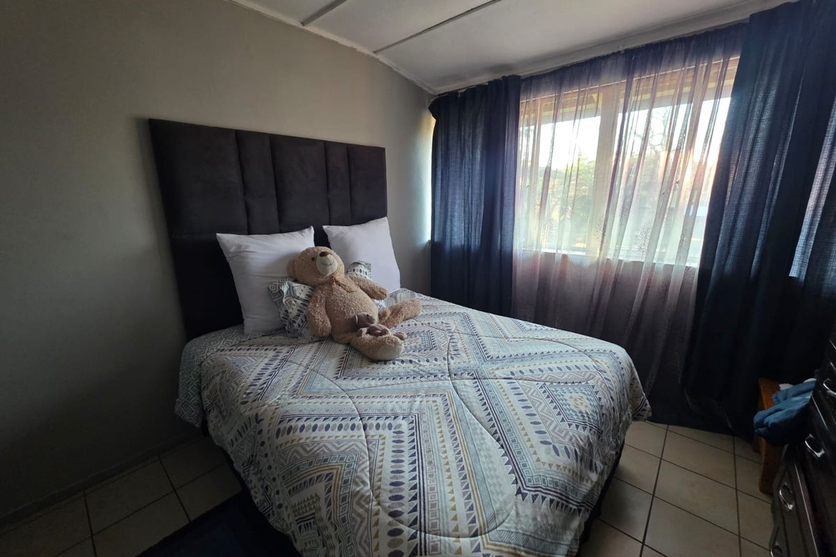 A bedroom featuring tiled flooring and a large window with curtains, providing natural light.