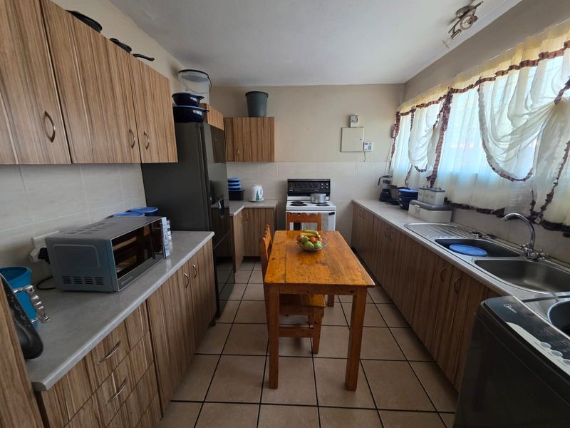 Functional kitchen featuring laminate cabinetry, tiled backsplash, double stainless steel sink, and a freestanding stove with ceramic floor tiles.