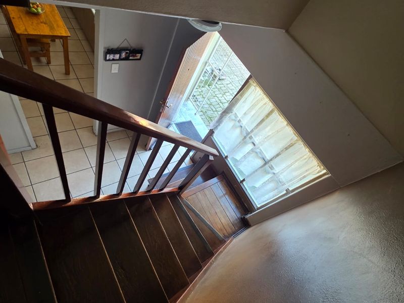A view looking down a wooden staircase towards the front entrance, featuring tiled flooring and a clear connection to the main living area.